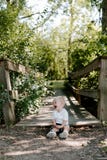 Cute Little Blond Haired Toddler Boy Kid Child Sitting And Laughing In Front Of Wooden Bridge Over A Creek At The Outdoor Park In Royalty Free Stock Image Cute Little Blond Haired Toddler Boy Kid Child Sitting And Laughing In Front Of Wooden Bridge Over A Creek At The Outdoor Park In Royalty Free Stock Image