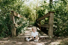 Cute Little Blond Haired Toddler Boy Kid Child Sitting And Laughing In Front Of Wooden Bridge Over A Creek At The Outdoor Park In Royalty Free Stock Images Cute Little Blond Haired Toddler Boy Kid Child Sitting And Laughing In Front Of Wooden Bridge Over A Creek At The Outdoor Park In Royalty Free Stock Images
