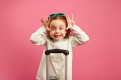 Cute little girl in sunglasses makes funny crazy face, big brown eyes, and raised arms stands near suitcase on isolated stock photography Cute little girl in sunglasses makes funny crazy face, big brown eyes, and raised arms stands near suitcase on isolated stock photography