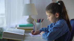 Cute little school girl doing homework at the table stock video footage Cute little school girl doing homework at the table stock video footage