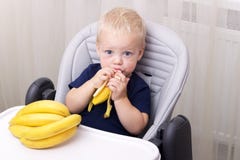Cute One Year Old Toddler Eating A Banana And Sitting In The Baby Chair. Royalty Free Stock Photos