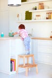 Cute toddler baby climbs on step stool, trying to reach things on the high desk in the kitchen. Cute toddler baby boy climbs on step stool, trying to reach Royalty Free Stock Photography Cute toddler baby climbs on step stool, trying to reach things on the high desk in the kitchen. Cute toddler baby boy climbs on step stool, trying to reach Royalty Free Stock Photography