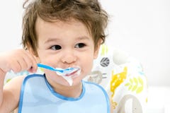 Cute toddler boy with blue spoon is yogurt. the child smiles. funny kid in a baby seat. beautiful 2 year old little boy eating Bre stock photo Cute toddler boy with blue spoon is yogurt. the child smiles. funny kid in a baby seat. beautiful 2 year old little boy eating Bre stock photo
