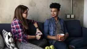 Cute young couple, attractive caucasian girl and her handsome mulatto boyfriend sitting on the couch, drinking tea stock video footage Cute young couple, attractive caucasian girl and her handsome mulatto boyfriend sitting on the couch, drinking tea stock video footage