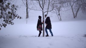 Cute young man and girl spend their leisure time in a snow-covered park. Date of young couple. Happy couple in love stock video Cute young man and girl spend their leisure time in a snow-covered park. Date of young couple. Happy couple in love stock video