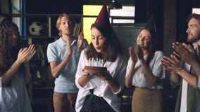 Cámara lenta de la señora joven feliz que sostiene la torta de cumpleaños y que sopla las velas que se colocan en oficina con los metrajes Cámara lenta de la señora joven feliz que sostiene la torta de cumpleaños y que sopla las velas que se colocan en oficina con los metrajes