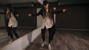 Dançarino fêmea novo na camisa branca, na calças preta e no tampão preto mostrando a jazz a dança moderna A menina está dançando filme Dançarino fêmea novo na camisa branca, na calças preta e no tampão preto mostrando a jazz a dança moderna A menina está dançando filme