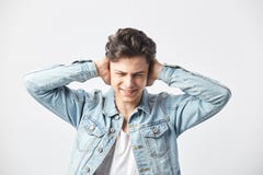 Dark-haired guy dressed in a white t-shirt and a denim jacket covers his ears with his hands on the white background in stock images Dark-haired guy dressed in a white t-shirt and a denim jacket covers his ears with his hands on the white background in stock images