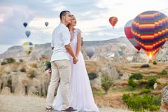 Data para w miłości przy zmierzchem przeciw tłu balony w Cappadocia, Turcja Mężczyzna i kobiety przytulenia pozycja na wzgórzu zdjęcia royalty free Data para w miłości przy zmierzchem przeciw tłu balony w Cappadocia, Turcja Mężczyzna i kobiety przytulenia pozycja na wzgórzu zdjęcia royalty free