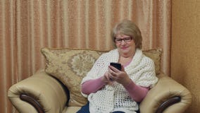 De aantrekkelijke glimlachende dame die een smartphone gebruiken, communiceert op Internet Gelukkige bejaardezitting in comfortab stock footage De aantrekkelijke glimlachende dame die een smartphone gebruiken, communiceert op Internet Gelukkige bejaardezitting in comfortab stock footage