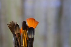 De artistieke gekleurde verf borstelt met wit, zwart en oranje varkenshaar op een groene vage achtergrond De werkplaats van stock foto De artistieke gekleurde verf borstelt met wit, zwart en oranje varkenshaar op een groene vage achtergrond De werkplaats van stock foto