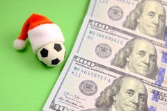 De bal van het herinneringsvoetbal in een rode Santa Claus-hoed naast dollars op een groene achtergrond Conceptensporten het wedd stock foto's De bal van het herinneringsvoetbal in een rode Santa Claus-hoed naast dollars op een groene achtergrond Conceptensporten het wedd stock foto's