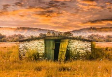 De bouw van de steenschuur op het grasgebied bij zonsondergang Verlaten oude loods in sprookjescène Gestileerde voorraadfoto met royalty-vrije stock afbeelding De bouw van de steenschuur op het grasgebied bij zonsondergang Verlaten oude loods in sprookjescène Gestileerde voorraadfoto met royalty-vrije stock afbeelding