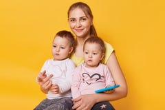 De charmante hartelijke brijzitting met haar leuke kleine dochters op vloer in gele studio, terloops geklede wijfjes, ziet eruit royalty-vrije stock foto's De charmante hartelijke brijzitting met haar leuke kleine dochters op vloer in gele studio, terloops geklede wijfjes, ziet eruit royalty-vrije stock foto's