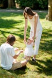 De charmante moeder en de gelukkige papa onderwijzen hun kleine dochter die witte kleding dragen hoe te om haar eerste stappen te stock foto De charmante moeder en de gelukkige papa onderwijzen hun kleine dochter die witte kleding dragen hoe te om haar eerste stappen te stock foto