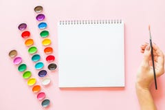 De creatieve vlakte legt van waterverfpaletten, notitieboekje, vrouwelijke de verfborstel van de handholding Kunstenaarswerkplaat stock afbeeldingen De creatieve vlakte legt van waterverfpaletten, notitieboekje, vrouwelijke de verfborstel van de handholding Kunstenaarswerkplaat stock afbeeldingen