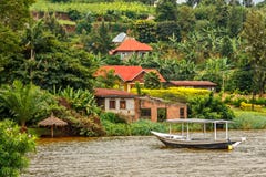 De dakboot verankerde bij de kust met Rwandees dorp op de achtergrond, Kivu-meer, Rwanda royalty-vrije stock afbeelding De dakboot verankerde bij de kust met Rwandees dorp op de achtergrond, Kivu-meer, Rwanda royalty-vrije stock afbeelding