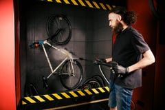 De diensten professionele was van een fiets in de workshop Een jonge Kaukasische modieuze mens met lang krullend haar doet een fi stock foto's De diensten professionele was van een fiets in de workshop Een jonge Kaukasische modieuze mens met lang krullend haar doet een fi stock foto's