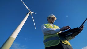 De energeticadeskundige navigeert zijn computer terwijl status dichtbij een windmolen Vernieuwbare alternatieve energie, milieu stock video De energeticadeskundige navigeert zijn computer terwijl status dichtbij een windmolen Vernieuwbare alternatieve energie, milieu stock video