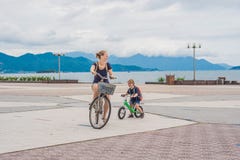 De gelukkige familie berijdt in openlucht fietsen en glimlacht Mamma op een fiets royalty-vrije stock afbeeldingen De gelukkige familie berijdt in openlucht fietsen en glimlacht Mamma op een fiets royalty-vrije stock afbeeldingen