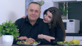 De gelukkige familie, meisje koestert haar papa en kijkt in camera thuis op keuken stock video De gelukkige familie, meisje koestert haar papa en kijkt in camera thuis op keuken stock video
