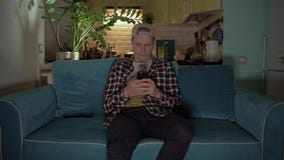 De gelukkige mens speelt spel op zijn mobiele telefoonzitting op de bank 4K stock footage De gelukkige mens speelt spel op zijn mobiele telefoonzitting op de bank 4K stock footage