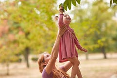 De gelukkige moeder loopt met het kind in het park in zonnige dag, aanraking en overweegt bladeren op een boom stock fotografie De gelukkige moeder loopt met het kind in het park in zonnige dag, aanraking en overweegt bladeren op een boom stock fotografie
