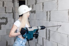 De het meisjesvoorman die van het close-upblonde in witte bouwhelm professionele perforator houden, boort binnenshuis in aanbouw royalty-vrije stock fotografie De het meisjesvoorman die van het close-upblonde in witte bouwhelm professionele perforator houden, boort binnenshuis in aanbouw royalty-vrije stock fotografie