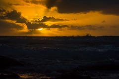 De het plaatsen zon stuurt stralen van achter de wolken over het breken van branding stock afbeelding De het plaatsen zon stuurt stralen van achter de wolken over het breken van branding stock afbeelding