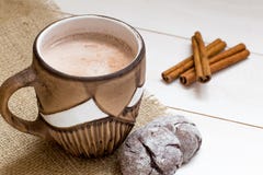 De hete cacao met melk in bruine kop, pijpjes kaneel op witte houten lijst, sluit omhoog stock foto De hete cacao met melk in bruine kop, pijpjes kaneel op witte houten lijst, sluit omhoog stock foto