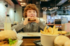 De hongerige jongen eet hamburger in restaurant royalty-vrije stock fotografie De hongerige jongen eet hamburger in restaurant royalty-vrije stock fotografie