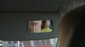 De jonge blonde vrouw schildert haar lippen in de auto kijkend aan achteruitkijkspiegel Langzame Motie stock video De jonge blonde vrouw schildert haar lippen in de auto kijkend aan achteruitkijkspiegel Langzame Motie stock video