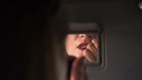 De jonge blonde vrouw schildert haar lippen in de auto De zon verlicht het gezicht Sluit omhoog stock footage De jonge blonde vrouw schildert haar lippen in de auto De zon verlicht het gezicht Sluit omhoog stock footage