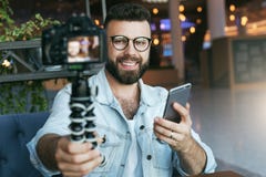 De jonge gebaarde mannelijke video blogger leidt tot videoinhoud voor zijn kanaal De gelukkige kerel schiet video stromend voor g stock afbeeldingen De jonge gebaarde mannelijke video blogger leidt tot videoinhoud voor zijn kanaal De gelukkige kerel schiet video stromend voor g stock afbeeldingen