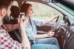 De jonge mens neemt beeld van meisjes drijfauto Hij doet dat gebruikend telefoon Het meisje houdt leidraad met haar handen en royalty-vrije stock fotografie De jonge mens neemt beeld van meisjes drijfauto Hij doet dat gebruikend telefoon Het meisje houdt leidraad met haar handen en royalty-vrije stock fotografie