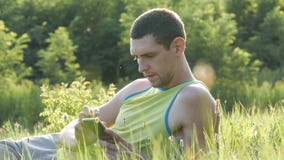 De jonge mens typt iets op zijn smartphone terwijl het zitten op aard op groen gras in de zomer stock videobeelden De jonge mens typt iets op zijn smartphone terwijl het zitten op aard op groen gras in de zomer stock videobeelden