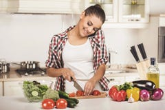 De jonge vrouw hakt groenten in de keuken en spreekt telefonisch royalty-vrije stock fotografie De jonge vrouw hakt groenten in de keuken en spreekt telefonisch royalty-vrije stock fotografie