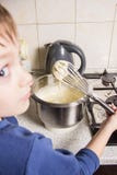 De jongen in de keuken kneedt het deeg voor cupcakes in de mixer, toevoegend ingrediënten stock afbeelding De jongen in de keuken kneedt het deeg voor cupcakes in de mixer, toevoegend ingrediënten stock afbeelding