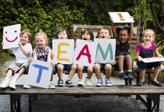 De kinderen zitten op de houten lijst houdend een woordteam royalty-vrije stock afbeeldingen De kinderen zitten op de houten lijst houdend een woordteam royalty-vrije stock afbeeldingen