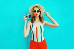 De kleurrijke jonge vrouw die retro camera houden, die rode lippen blazen verzendt luchtkus in de hoed die van het de zomerstro p stock fotografie De kleurrijke jonge vrouw die retro camera houden, die rode lippen blazen verzendt luchtkus in de hoed die van het de zomerstro p stock fotografie