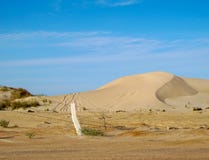 De kustzandduinen met bandsporen en het prikkeldraad schermen tegen blauwe hemel in Libië stock fotografie De kustzandduinen met bandsporen en het prikkeldraad schermen tegen blauwe hemel in Libië stock fotografie