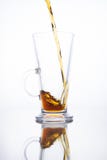 De la bière foncée est versée dans une tasse vide sur un fond blanc Fluide d'éclaboussure image stock De la bière foncée est versée dans une tasse vide sur un fond blanc Fluide d'éclaboussure image stock