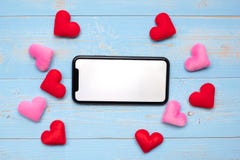 De lege touchscreen vertoning van zwarte smartphone met rode en roze harten vormt decoratie op blauwe houten lijstachtergrond Lie stock foto's De lege touchscreen vertoning van zwarte smartphone met rode en roze harten vormt decoratie op blauwe houten lijstachtergrond Lie stock foto's