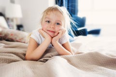 De leuke gelukkige zitting van het peutermeisje op bed in pyjama Kind dat thuis speelt royalty-vrije stock foto De leuke gelukkige zitting van het peutermeisje op bed in pyjama Kind dat thuis speelt royalty-vrije stock foto