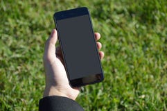 De mannelijke smartphone van de handholding met grasachtergrond royalty-vrije stock afbeelding De mannelijke smartphone van de handholding met grasachtergrond royalty-vrije stock afbeelding