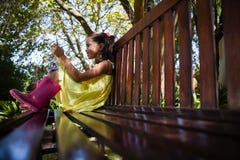De mening van het oppervlakteniveau van glimlachend meisje die mobiele telefoon met behulp van terwijl het zitten op houten bank royalty-vrije stock foto De mening van het oppervlakteniveau van glimlachend meisje die mobiele telefoon met behulp van terwijl het zitten op houten bank royalty-vrije stock foto