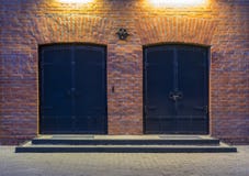De mening van de nacht Zaken - de Horizon van de Stad van Nietjes Twee grote metaaldeuren in een rood baksteengebouw De ingang aa stock foto's De mening van de nacht Zaken - de Horizon van de Stad van Nietjes Twee grote metaaldeuren in een rood baksteengebouw De ingang aa stock foto's