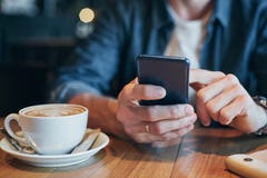 De mens dient de dia van het denimoverhemd met vinger op het scherm zijn smartphone, dichtbij kop met koffie op houten lijst in royalty-vrije stock fotografie De mens dient de dia van het denimoverhemd met vinger op het scherm zijn smartphone, dichtbij kop met koffie op houten lijst in royalty-vrije stock fotografie