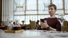 De mens zit bij lijst in restaurant, kijkt op een rekening en verricht betaling door kaart De kelner houdt terminal in handen stock footage De mens zit bij lijst in restaurant, kijkt op een rekening en verricht betaling door kaart De kelner houdt terminal in handen stock footage