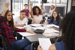 De middelbare schooljonge geitjes heffen handen, leraarszitting bij hun bureau op royalty-vrije stock foto's De middelbare schooljonge geitjes heffen handen, leraarszitting bij hun bureau op royalty-vrije stock foto's